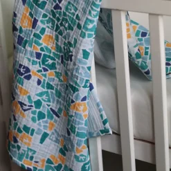 türkiz színű mintás babatakaró rácsos ágyra terítve